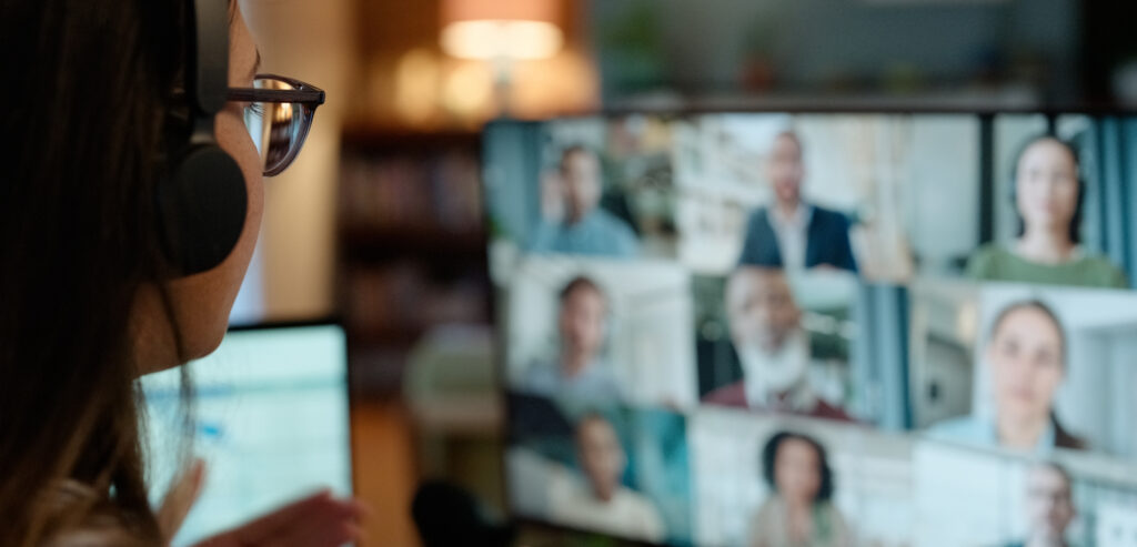 Woman looking at a computer monitor displaying multiple people in a virtual webinar meeting.